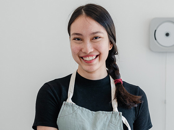 Young woman with her hair tied back in a braid and wearing an apron smiles at the camera
