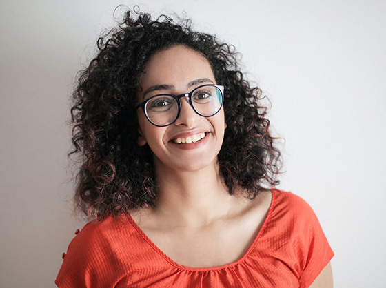 Woman wearing glasses and an orange shirt smiles at the camera